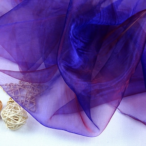 May include: A sheer fabric with a gradient of purple and red colors. The fabric is translucent and has a soft, flowing texture.