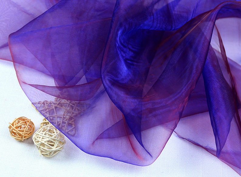 May include: A sheer fabric with a gradient of purple and red colors. The fabric is translucent and has a soft, flowing texture.