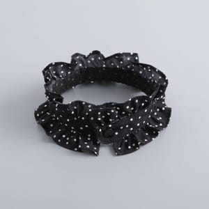 May include: Black and white polka dot ruffled collar with a button closure. The collar is made of a lightweight fabric and features a delicate, ruffled edge. The white polka dots are evenly spaced across the black background.