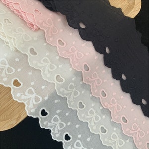 Peut inclure: Quatre bobines de dentelle blanche, rose et noire avec un bord festonné et des nœuds brodés.