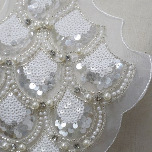 May include: White beaded and sequined applique with a scalloped edge. The applique is made of white sequins, pearls, and rhinestones.