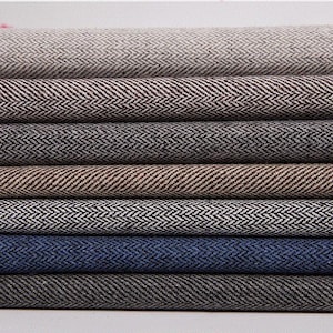 Può includere: Una pila di campioni di tessuto a spina di pesce di vari colori. I colori includono sfumature di grigio, marrone e blu. Il tessuto ha una trama tessuta e viene probabilmente utilizzato per abbigliamento o tappezzeria.