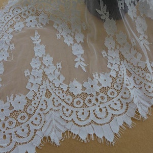 Puede incluir: Borde de encaje blanco con un delicado patr&oacute;n floral y un borde festoneado. El encaje es transparente y tiene una textura suave y fluida.