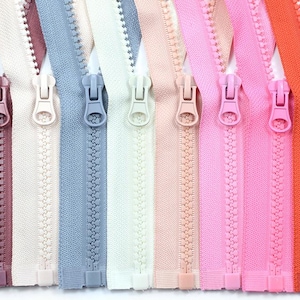 Pode incluir: Uma coleção de zíperes coloridos em várias tonalidades, incluindo rosa, laranja, azul e branco. Cada zíper está fechado, mostrando o puxador e os dentes. Os zíperes estão dispostos lado a lado, destacando a gama de cores disponíveis para costura e artesanato.