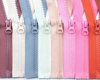 May include: A collection of colorful zippers in various shades, including pink, orange, blue, and white. Each zipper is closed, showcasing the pull tab and teeth. The zippers are arranged side by side, highlighting the range of colors available for sewing and crafting projects.
