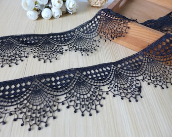 May include: Black lace trim with a scalloped edge and a delicate pattern. The lace is about 2 inches wide and has a soft, flowing texture.
