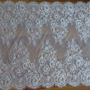 May include: White lace fabric with a delicate floral pattern. The lace has a scalloped edge and is sheer.