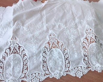 May include: White cotton fabric with a delicate white lace trim. The lace features a repeating pattern of oval shapes with floral embroidery.