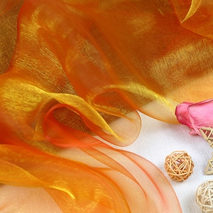 May include: Orange and yellow sheer fabric with a pink rose and a woven star on a white background.
