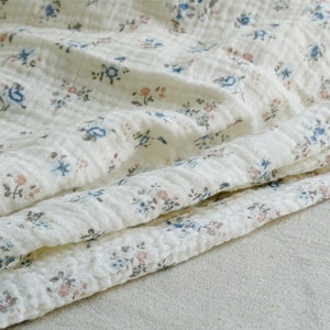 May include: White cotton fabric with a small floral print in shades of blue and pink. The fabric is textured and has a slightly wrinkled appearance.