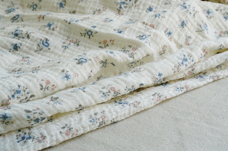 May include: White cotton fabric with a small floral print in shades of blue and pink. The fabric is textured and has a slightly wrinkled appearance.
