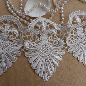May include: White lace trim with a delicate floral pattern. The lace has a scalloped edge and is perfect for adding a touch of elegance to any project.