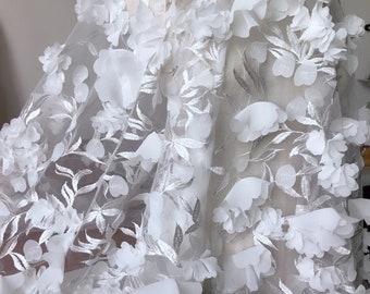 May include: White floral lace fabric with 3D flowers. The fabric has a delicate, sheer texture and is perfect for adding a touch of elegance to any project.