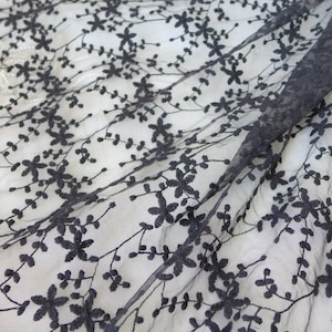 K&ouml;nnte beinhalten: Schwarzer Blumenspitzenstoff mit einem zarten Muster aus kleinen Bl&uuml;ten und Bl&auml;ttern. Die Spitze ist durchsichtig und hat eine weiche, flie&szlig;ende Textur.