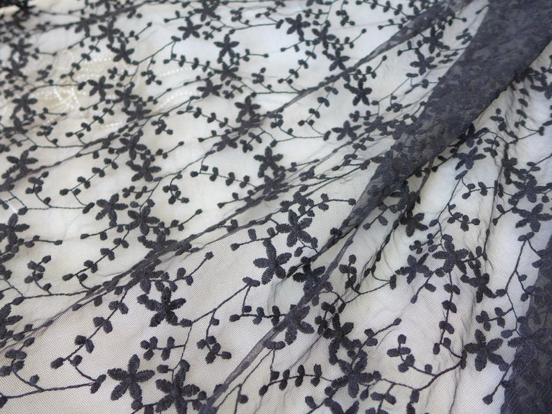 K&ouml;nnte beinhalten: Schwarzer Blumenspitzenstoff mit einem zarten Muster aus kleinen Bl&uuml;ten und Bl&auml;ttern. Die Spitze ist durchsichtig und hat eine weiche, flie&szlig;ende Textur.