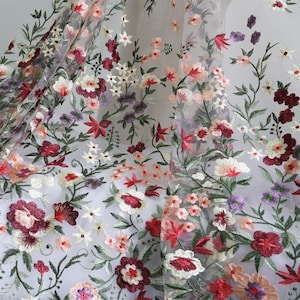 May include: Delicate sheer fabric adorned with detailed floral embroidery. The design showcases a range of flowers in red, pink, white, and purple, with green stems and leaves. The fabric is lightweight and suitable for clothing or decorative purposes.