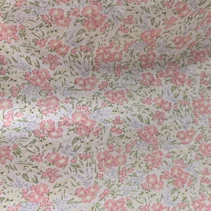 Puede incluir: Primer plano de una tela con estampado floral. El patr&oacute;n presenta grupos de flores rosas con hojas verdes y peque&ntilde;as flores azules sobre un fondo blanco. La tela tiene una est&eacute;tica delicada y vintage.
