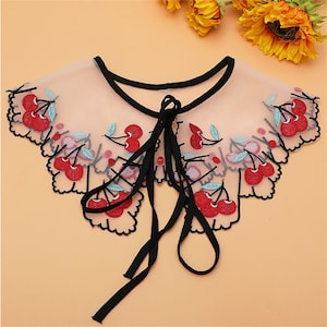 May include: A delicate sheer black lace collar with a cherry embroidery design. The collar has a black ribbon tie.