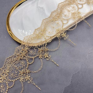 May include: Gold lace trim with a delicate floral pattern and a scalloped edge. The lace is on a sheer mesh background.