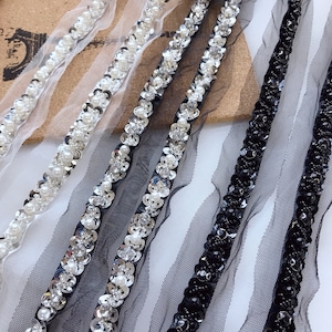 May include: Three different trims of black and white beaded and sequined trim on a sheer mesh fabric. The trim is approximately 1 inch wide.