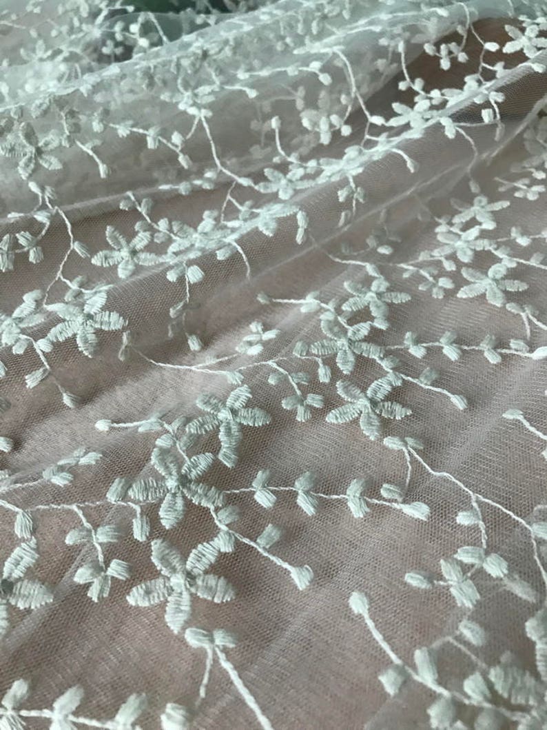 K&ouml;nnte beinhalten: Wei&szlig;e florale Stickerei auf einem durchsichtigen, hellgr&uuml;nen Stoff. Der Stoff hat eine zarte, luftige Haptik und ist perfekt zum Basteln oder um jedem Projekt einen Hauch von Eleganz zu verleihen.