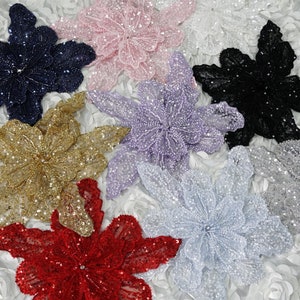 May include: Assortment of six sparkly flower embellishments in various colours, including navy blue, pink, lavender, gold, silver, and red. Each flower is made of sequins and beads.