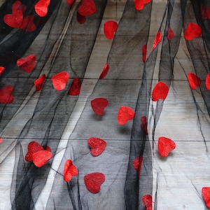 May include: Black tulle fabric with red heart-shaped embellishments. The fabric is draped over a wooden surface.