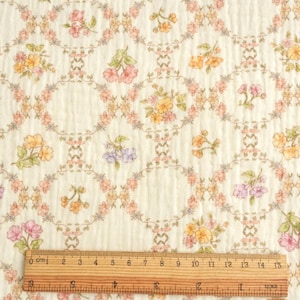 May include: Cream-colored fabric with a floral pattern. The design features oval frames with pink, yellow, and purple flowers, connected by a delicate vine-like pattern. A wooden ruler shows measurements up to 15 inches.