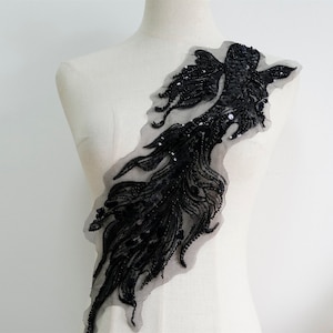 May include: Black beaded and sequined applique in the shape of a fish tail. The applique is on a sheer mesh fabric.