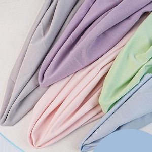 May include: A collection of soft fabric pieces in pastel shades, including light gray, lavender, pale pink, mint green, and baby blue. The textiles are arranged in overlapping folds, showcasing a smooth, matte texture and consistent drape.