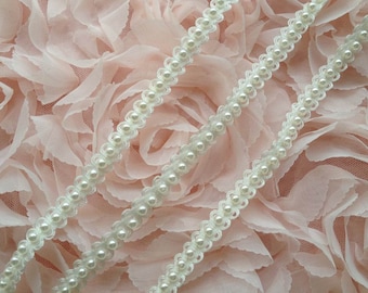 May include: Two white pearl trim embellishments on a pink fabric background. The trim features small white pearls sewn onto a white lace base.