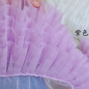 May include: Close-up of a lavender tulle fabric with multiple layers of ruffles. The fabric is soft and delicate, with a fine mesh texture.
