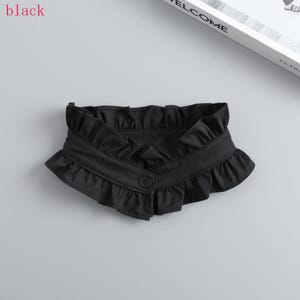 May include: A black ruffled collar with a button closure. The collar is made of a soft fabric and features a decorative ruffle along the edges. The word "black" is in the top left corner.