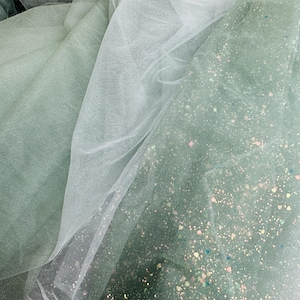 Może przedstawiać: Dwie warstwy przezroczystego materiału, jedna biała, a druga zielona z mieniącym się brokatem, są ułożone jedna na drugiej. Zielony materiał ma subtelny połysk.