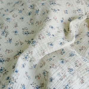 May include: A white fabric with a small floral pattern in shades of blue, brown, and pink. The fabric is textured and has a crinkled appearance.