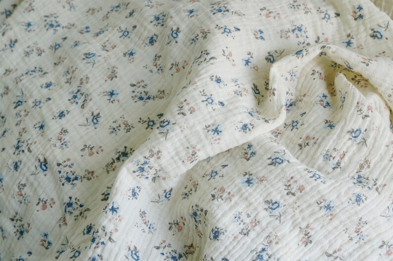 May include: A white fabric with a small floral pattern in shades of blue, brown, and pink. The fabric is textured and has a crinkled appearance.