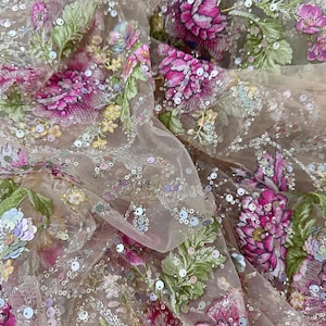 Könnte beinhalten: Nahaufnahme eines transparenten Stoffes mit aufwendiger Blumenstickerei. Das Design zeigt große, leuchtend rosa Blüten, grüne Blätter und zarte Pailletten. Der Stoff hat ein weiches, fließendes Aussehen, ideal für Kleider oder Dekorationsprojekte.