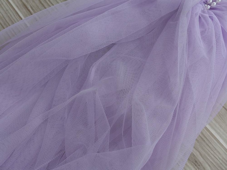 May include: A piece of soft, lilac tulle fabric with a delicate, fine mesh texture. The fabric is draped and folded, creating a soft, flowing look.