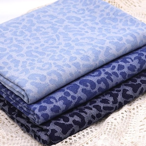 May include: A pile of blue patterned fabric, with a leopard print design. The fabric is in shades of blue, from light to dark. The layers are neatly folded and stacked. The material appears to be denim or a similar fabric.