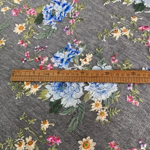 Puede incluir: Tela gris con un patr&oacute;n floral con flores azules, blancas y rosas. Una regla de madera con marcas en pulgadas se coloca sobre la tela.