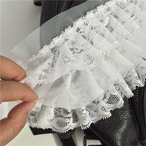 May include: White lace trim with a ruffled edge. The lace is delicate and has a floral pattern. The trim is perfect for adding a touch of elegance to any project.