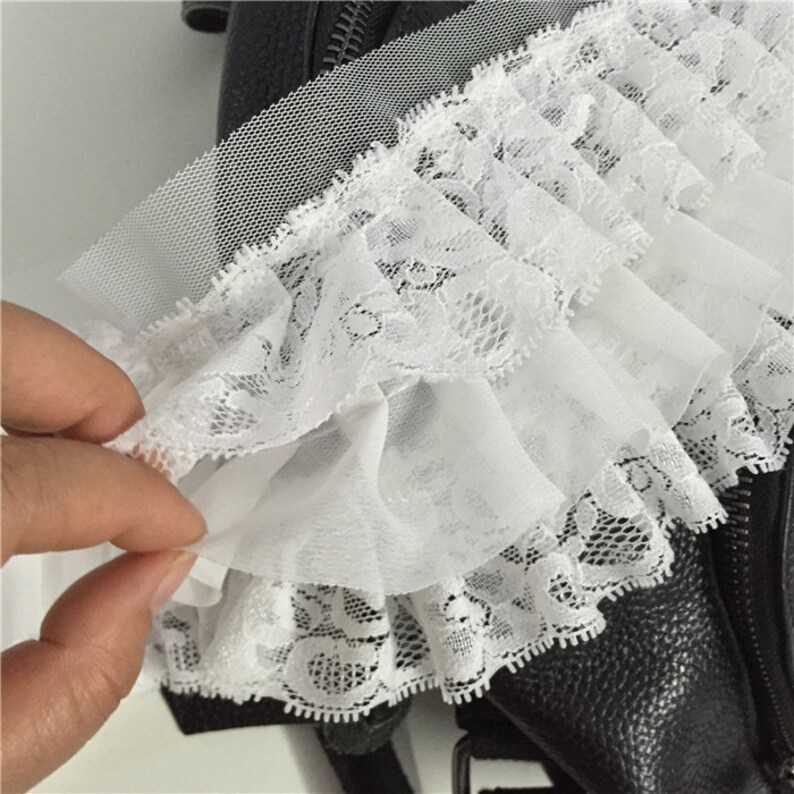 May include: White lace trim with a ruffled edge. The lace is delicate and has a floral pattern. The trim is perfect for adding a touch of elegance to any project.