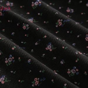 Pu&ograve; includere: Primo piano di tessuto nero con motivo floreale. Il tessuto ha una trama a coste ed &egrave; adornato da piccoli disegni floreali sparsi in tonalit&agrave; di rosa, blu e verde. La parola "black" &egrave; visibile nell'angolo in alto a sinistra.