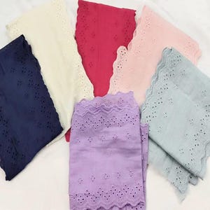 Puede incluir: Una colección de piezas de tela calada de colores variados, incluyendo azul marino, crema, rojo, rosa, lavanda y azul claro. Cada pieza tiene un borde festoneado y pequeños patrones decorativos recortados, creando una apariencia delicada y texturizada.