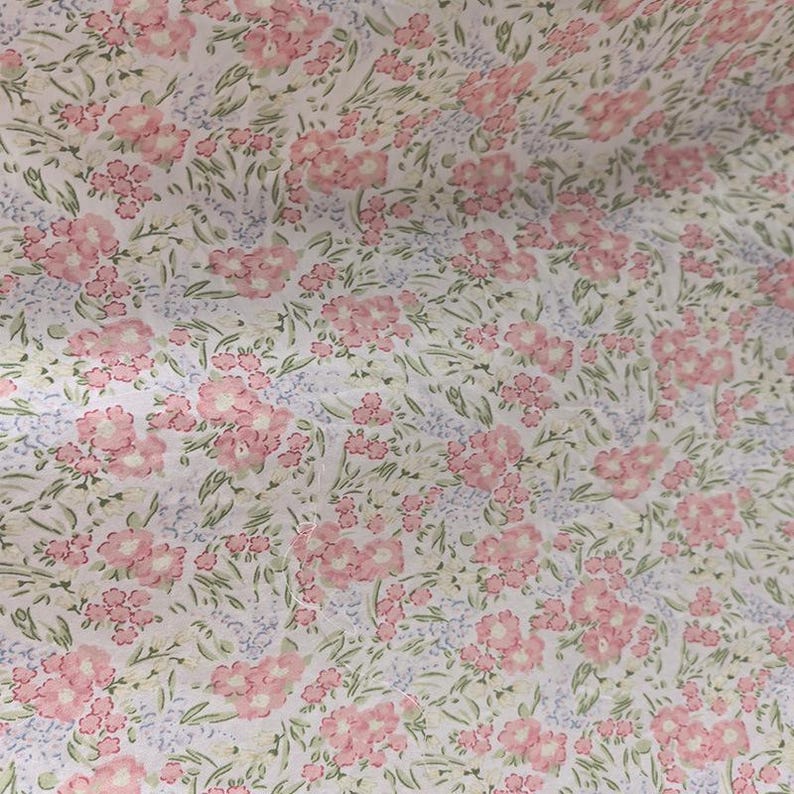 Puede incluir: Una tela con un estampado floral repetido. El dise&ntilde;o presenta grupos de flores rosas, peque&ntilde;as flores azules y hojas verdes sobre un fondo blanco. El efecto general es delicado y femenino.