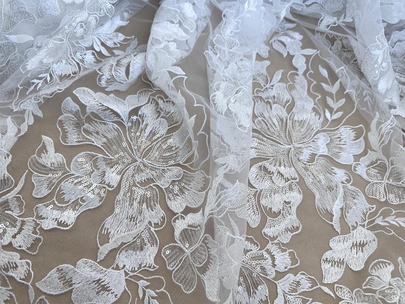 May include: White floral lace fabric with sequins. The lace features a delicate floral pattern with a sheer background.