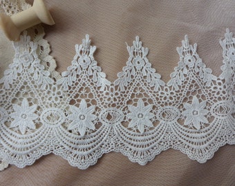 Puede incluir: Borde de encaje blanco con un borde festoneado y un diseño floral. El encaje es delicado e intrincado, con un toque suave y femenino.