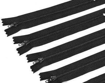 May include: A set of five black zips arranged diagonally across the frame. Each zip features a black fabric tape, black plastic teeth, and a black metal slider pull. The zips are positioned parallel to one another in a repeating pattern.