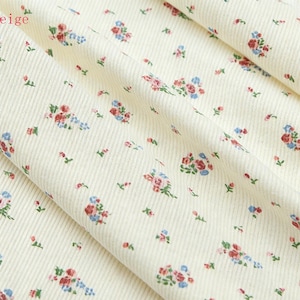 Pu&ograve; includere: Primo piano di tessuto di velluto a coste beige con motivo floreale. Il tessuto presenta piccoli gruppi di fiori rossi, blu e rosa con foglie verdi sparse sulla superficie. La parola "beige" &egrave; nell'angolo in alto a sinistra.
