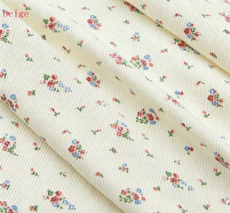 Pu&ograve; includere: Primo piano di tessuto di velluto a coste beige con motivo floreale. Il tessuto presenta piccoli gruppi di fiori rossi, blu e rosa con foglie verdi sparse sulla superficie. La parola "beige" &egrave; nell'angolo in alto a sinistra.